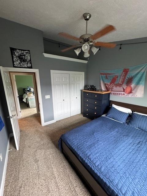 bedroom featuring a textured ceiling, carpet floors, a closet, baseboards, and a ceiling fan
