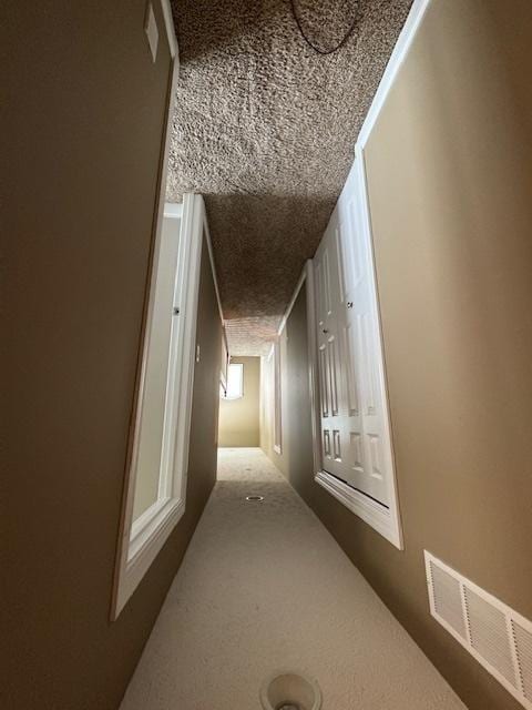 hallway featuring visible vents, carpet floors, and a textured ceiling