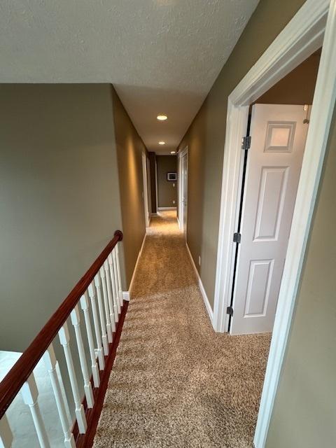 hall with a textured ceiling, carpet flooring, and baseboards