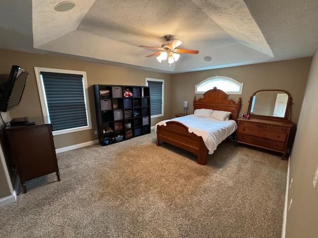 carpeted bedroom with baseboards, a raised ceiling, a ceiling fan, and a textured ceiling
