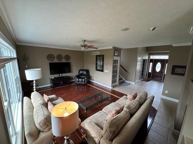 living room with stairs, ornamental molding, ceiling fan, baseboards, and a textured ceiling
