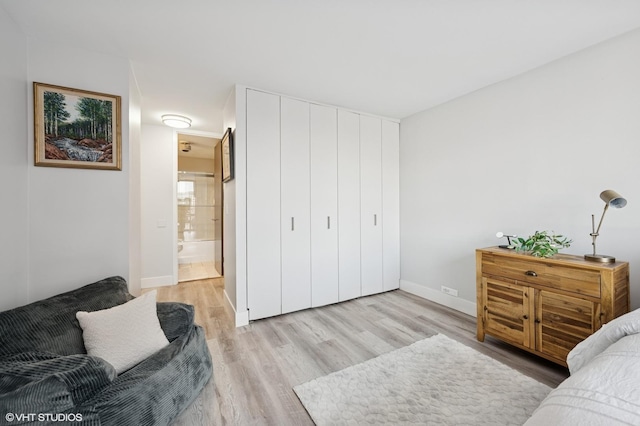 bedroom with a closet, baseboards, ensuite bath, and light wood-style floors