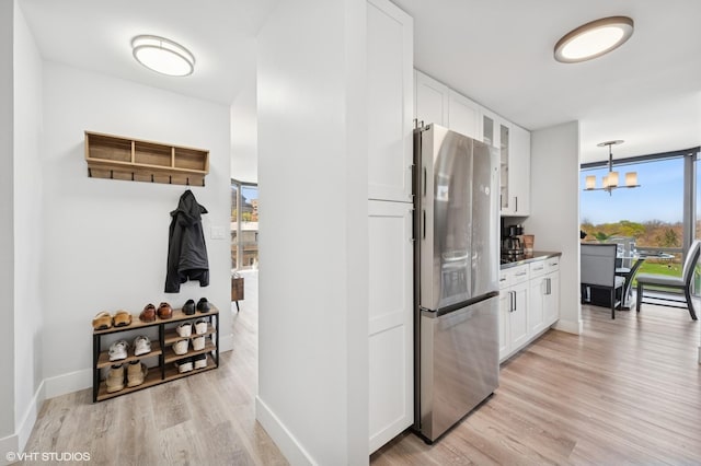 kitchen with glass insert cabinets, freestanding refrigerator, a notable chandelier, light wood-style floors, and white cabinetry