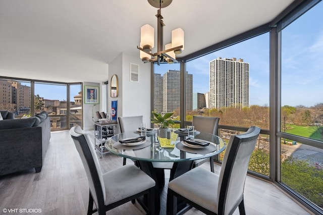 dining area with a wall of windows, a view of city, wood finished floors, and a chandelier