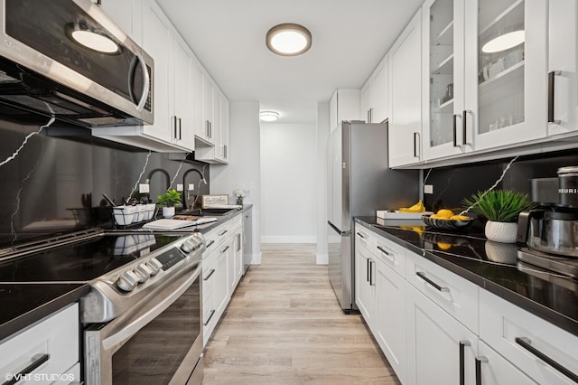 kitchen with a sink, appliances with stainless steel finishes, white cabinets, and light wood-style floors