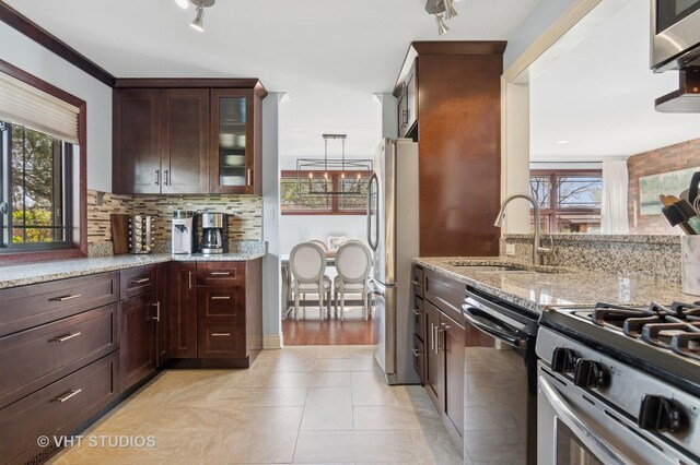 kitchen with stainless steel appliances, a sink, decorative backsplash, and light stone countertops