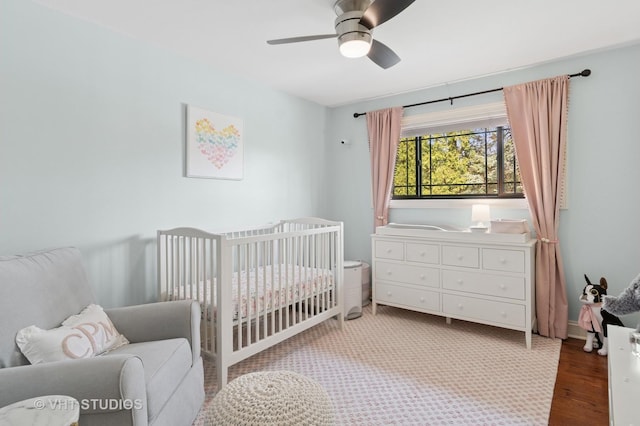 bedroom with a crib, wood finished floors, and ceiling fan