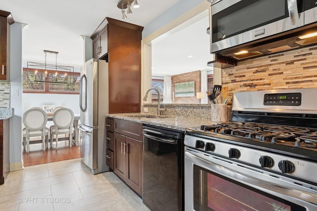 kitchen featuring appliances with stainless steel finishes, a sink, backsplash, light stone countertops, and dark brown cabinets