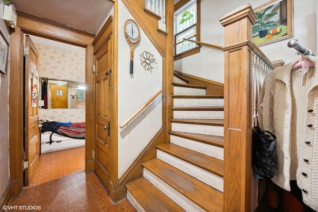 staircase featuring brick patterned floor and wallpapered walls