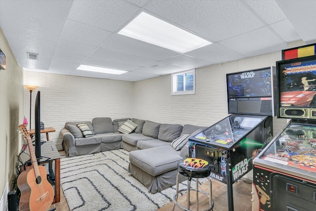 living area with brick wall, visible vents, and a drop ceiling