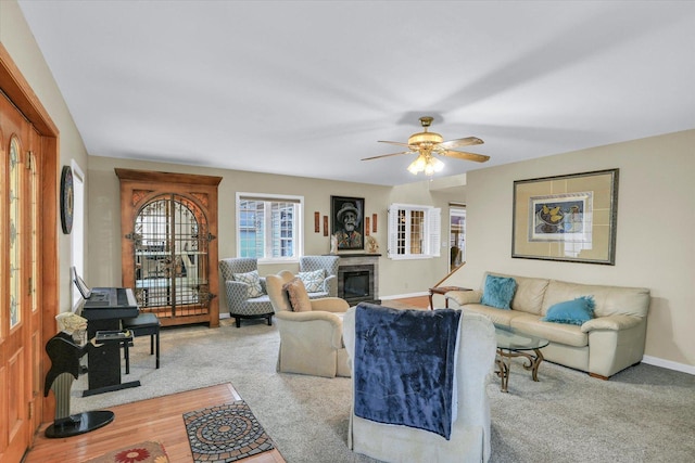 living area with ceiling fan, a glass covered fireplace, baseboards, and carpet