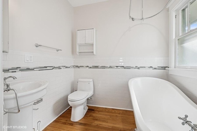 full bath with a freestanding tub, tile walls, wainscoting, and toilet