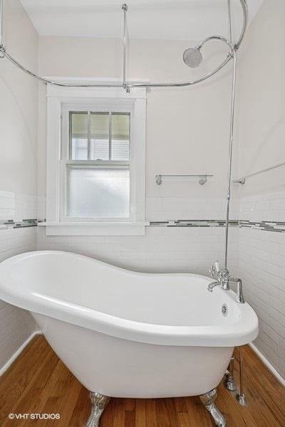 bathroom with a freestanding tub, tile walls, wainscoting, and wood finished floors