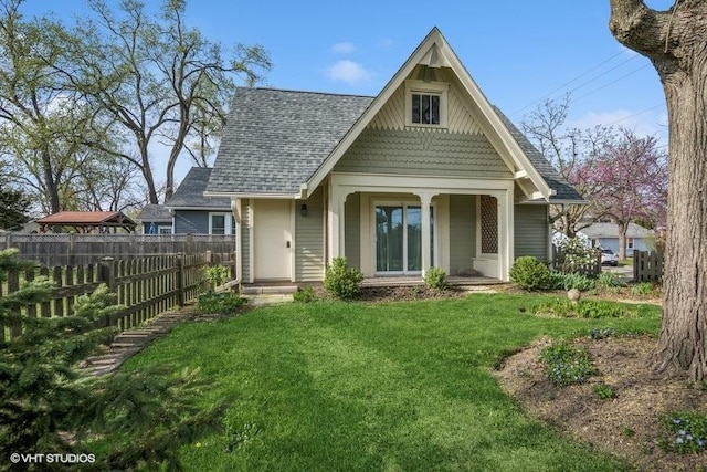 back of house featuring a lawn, fence, a shingled roof, and a porch