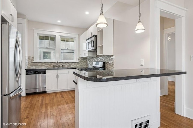 kitchen featuring a peninsula, dark countertops, light wood-type flooring, a sink, and stainless steel appliances
