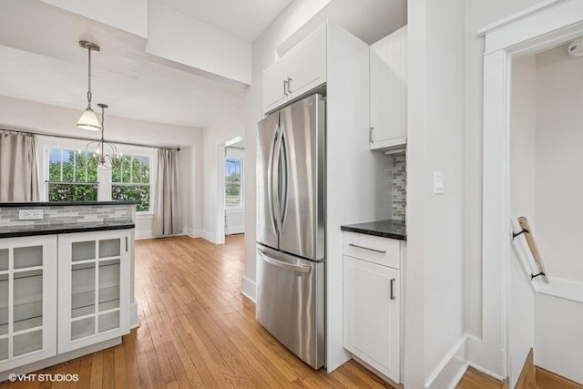 kitchen with dark countertops, hanging light fixtures, light wood-type flooring, white cabinets, and freestanding refrigerator