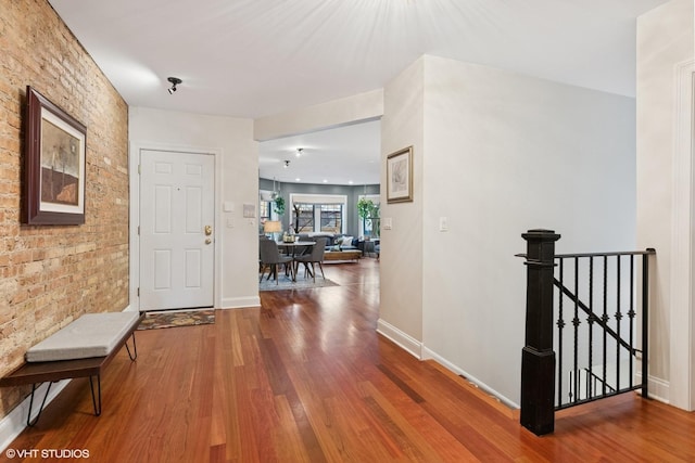 corridor with baseboards, wood finished floors, brick wall, and an upstairs landing