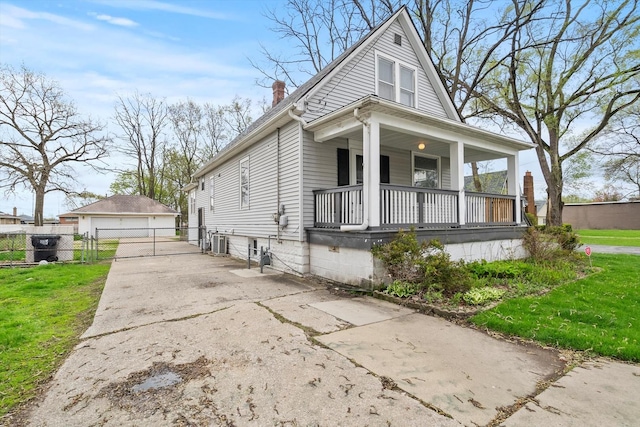 shotgun-style home with covered porch, a chimney, an outbuilding, fence, and a front lawn