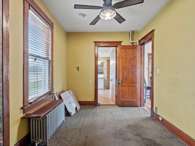 unfurnished room featuring radiator heating unit, baseboards, ceiling fan, and carpet