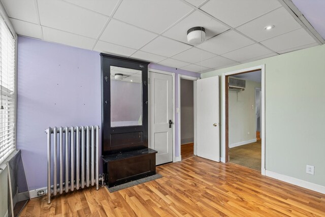 interior space with baseboards, a wall mounted AC, radiator heating unit, and light wood finished floors