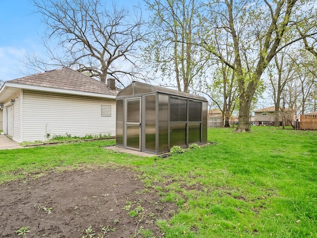 rear view of property featuring a lawn, an outbuilding, fence, and a greenhouse