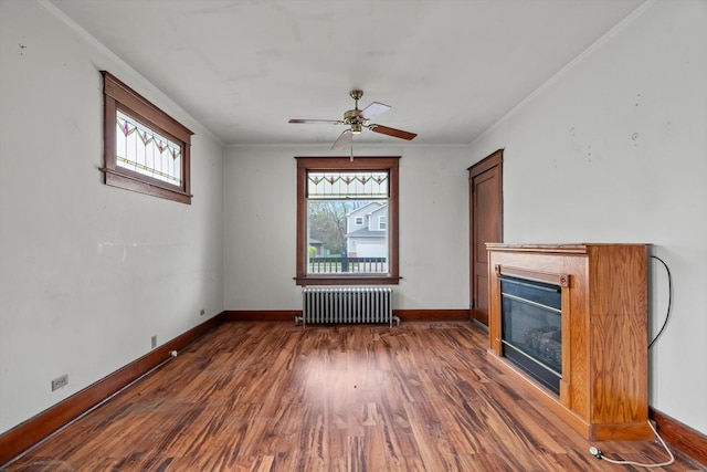 unfurnished living room with ceiling fan, wood finished floors, baseboards, a glass covered fireplace, and radiator heating unit