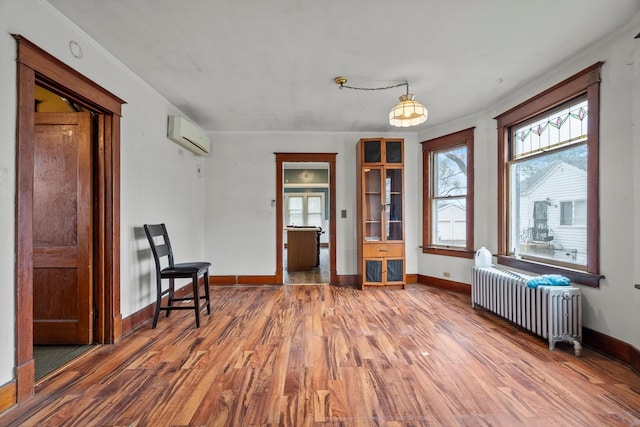 sitting room featuring wood finished floors, baseboards, a wall unit AC, and radiator heating unit