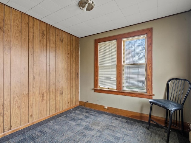 spare room with baseboards, dark colored carpet, and wood walls
