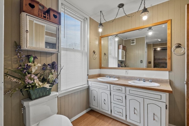 bathroom featuring visible vents, a sink, wood finished floors, and wood walls