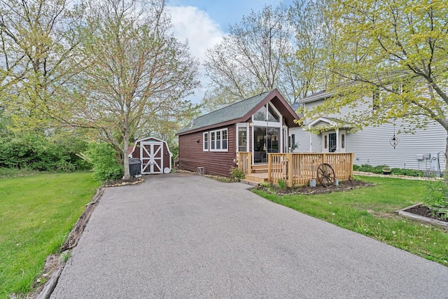 view of front facade featuring a wooden deck, an outbuilding, a shed, and a front yard