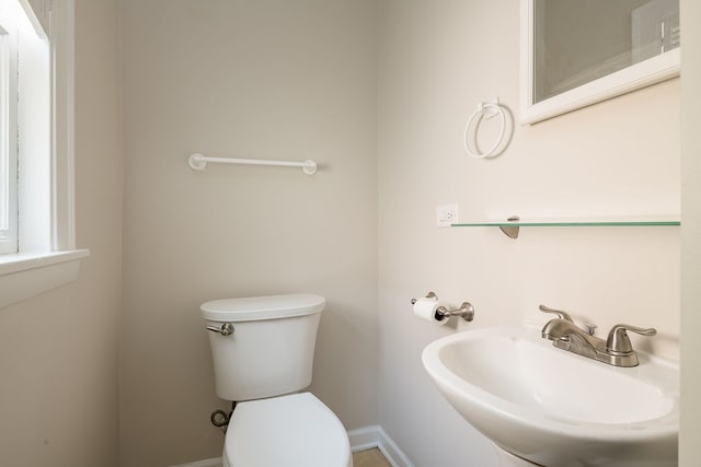 half bath featuring toilet, baseboards, and a sink