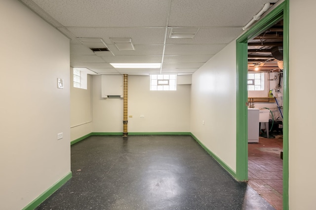 basement featuring a paneled ceiling, baseboards, a wealth of natural light, and washer / clothes dryer