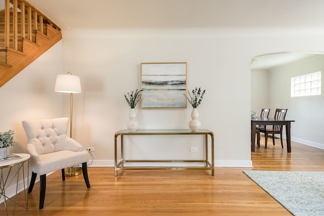 sitting room featuring stairs, arched walkways, baseboards, and wood finished floors