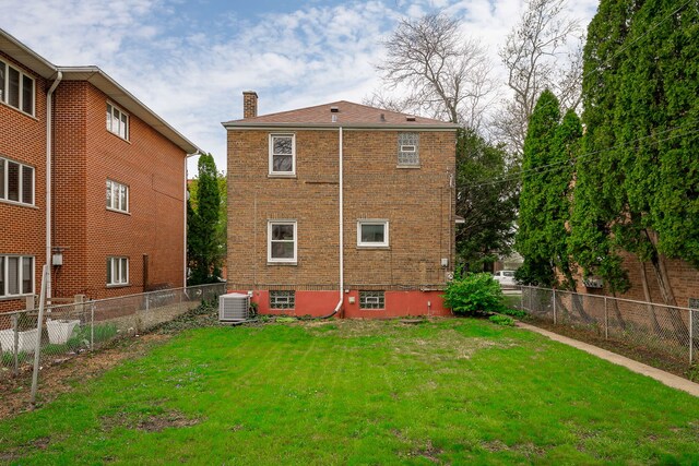 back of property featuring a fenced backyard, a chimney, a yard, and brick siding
