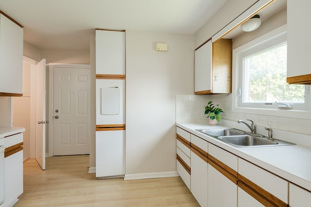 kitchen featuring backsplash, a sink, light countertops, white cabinets, and light wood-style flooring