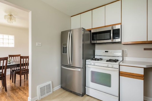 kitchen with appliances with stainless steel finishes, light wood-type flooring, white cabinetry, and visible vents