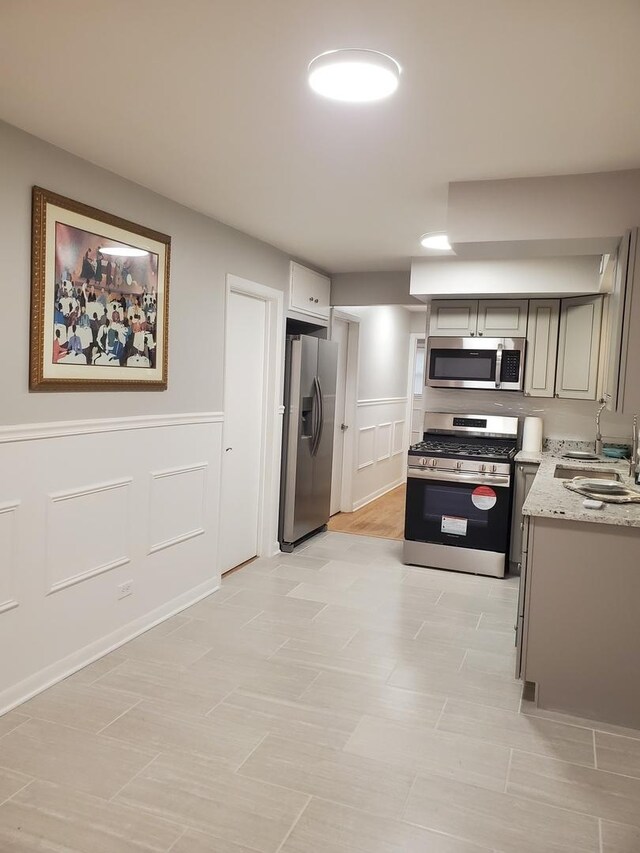 530 E 91st Pl, Chicago, IL 60619 - kitchen with light stone countertops, a decorative wall, stainless steel appliances, a wainscoted wall, and a sink
