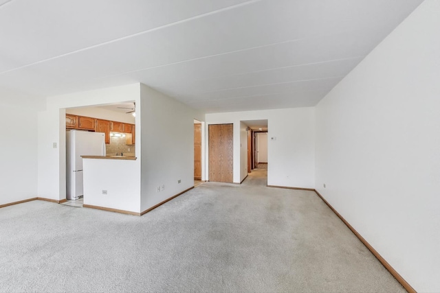 unfurnished living room featuring baseboards, a ceiling fan, and light colored carpet
