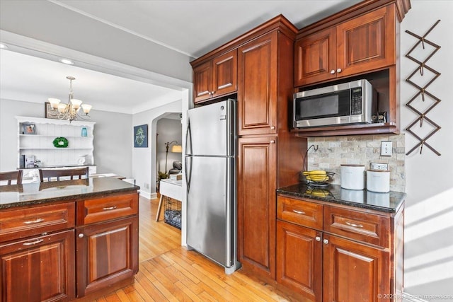 kitchen featuring tasteful backsplash, arched walkways, light wood-style flooring, a notable chandelier, and stainless steel appliances