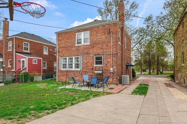back of property with fence, a chimney, brick siding, central AC unit, and a lawn