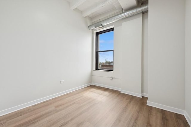 spare room with baseboards, beam ceiling, and light wood-type flooring
