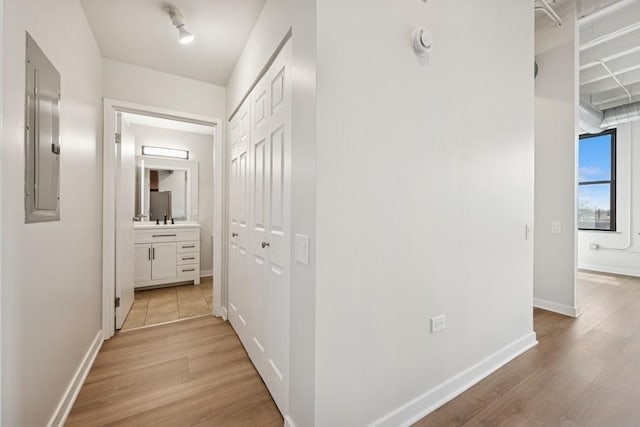 hall with light wood-style floors, baseboards, electric panel, and a sink