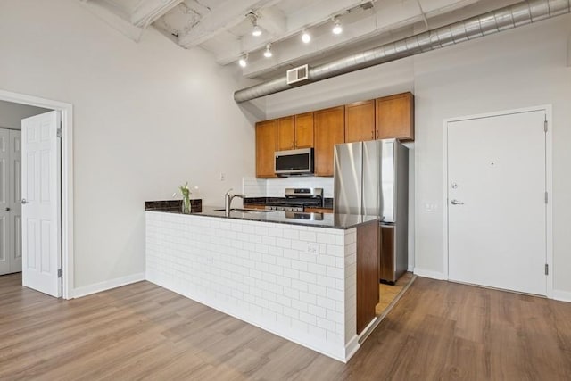 kitchen featuring dark countertops, brown cabinetry, stainless steel appliances, a peninsula, and visible vents