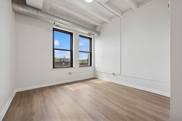 empty room with baseboards, beam ceiling, wood finished floors, and visible vents