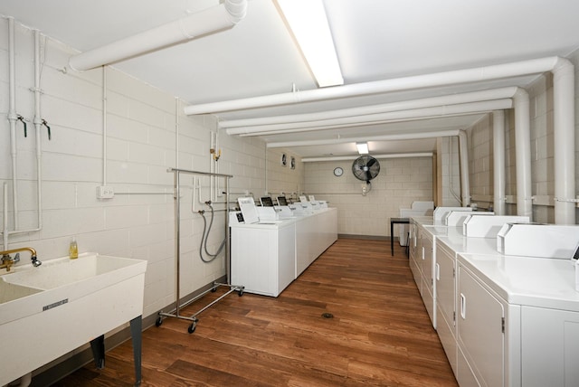 common laundry area with concrete block wall, washing machine and dryer, a sink, and dark wood-type flooring