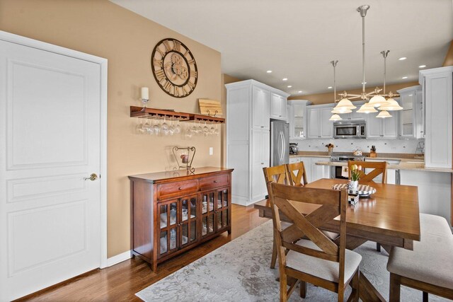 dining area featuring recessed lighting, a bar, wood finished floors, and baseboards