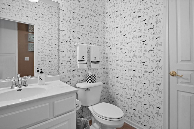 half bath featuring baseboards, wallpapered walls, toilet, and vanity
