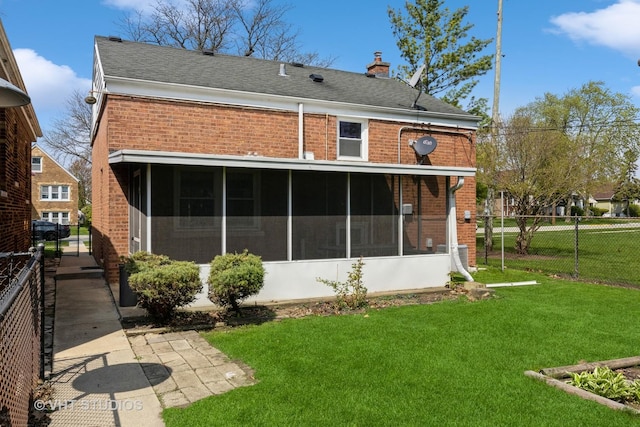 rear view of house with fence, brick siding, a sunroom, a chimney, and a yard