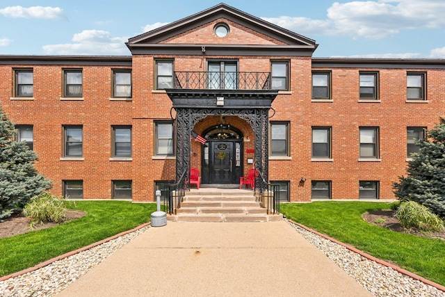 view of front of house with brick siding, a front lawn, and a balcony