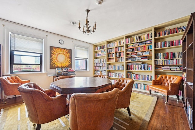 living area with an inviting chandelier, wall of books, and wood finished floors